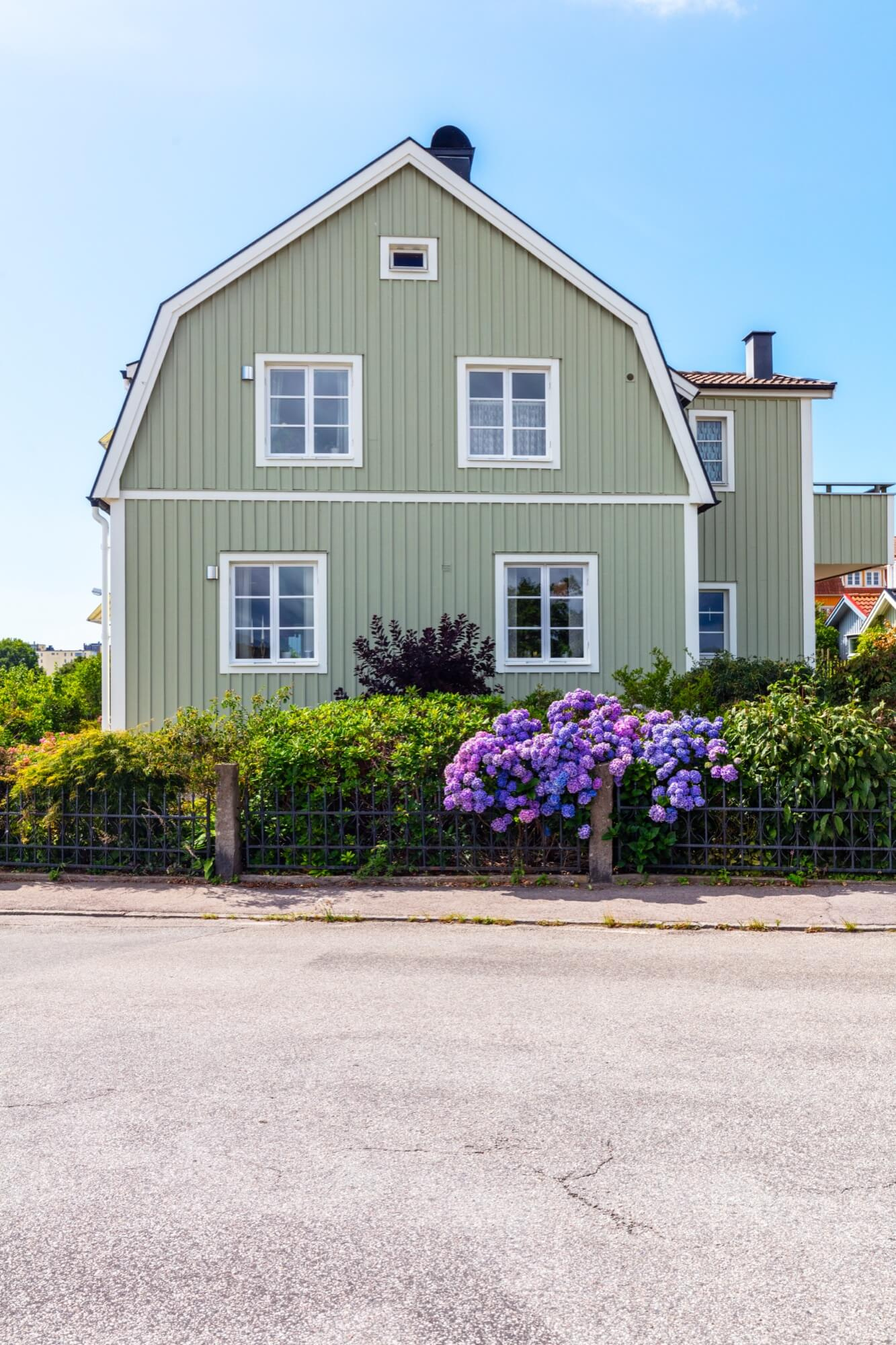 En klassisk svensk villa med ljusgrön träpanel och blommande trädgård, där en entreprenad kan ha innefattat renovering.