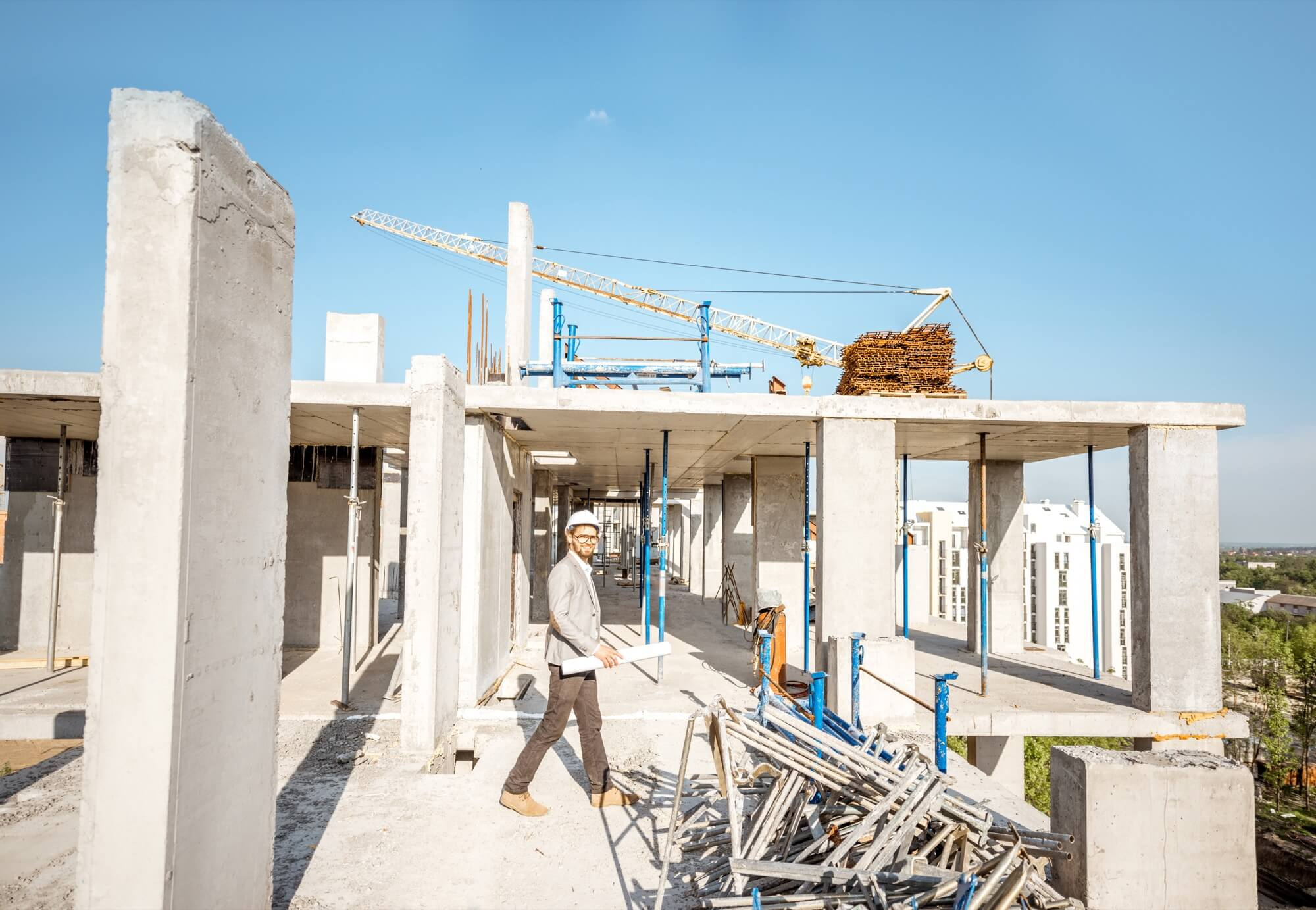 En ingenjör med bygghjälm och ritningar övervakar ett stort byggprojekt, en betongstomme under entreprenad.